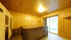 Een houten kamer met een jacuzzi, houten wanden, een schuifglazen deur en een plafondlamp.