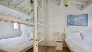 A room with two beds, a wooden floor, a white wardrobe, and a painting on the wall. - Florentine Gem Apartment (Firenze)