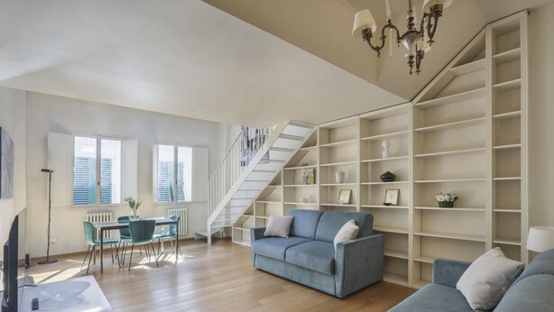 A spacious living room with a blue sofa, a dining area with a table and chairs, and a staircase leading to another level. - Florentine Gem Apartment (Firenze)