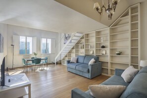 A spacious living room with a blue sofa, a dining area with a table and chairs, and a staircase leading to another level. - Florentine Gem Apartment (Firenze)