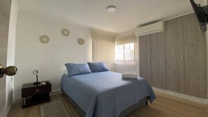 A bedroom with a bed, a wardrobe, a bedside table, and a window with blinds. - Apartamento Amplio, Tranquilo , Cómodo y Seguro a 5 min de CC Buenavista, Viva (Barranquilla)