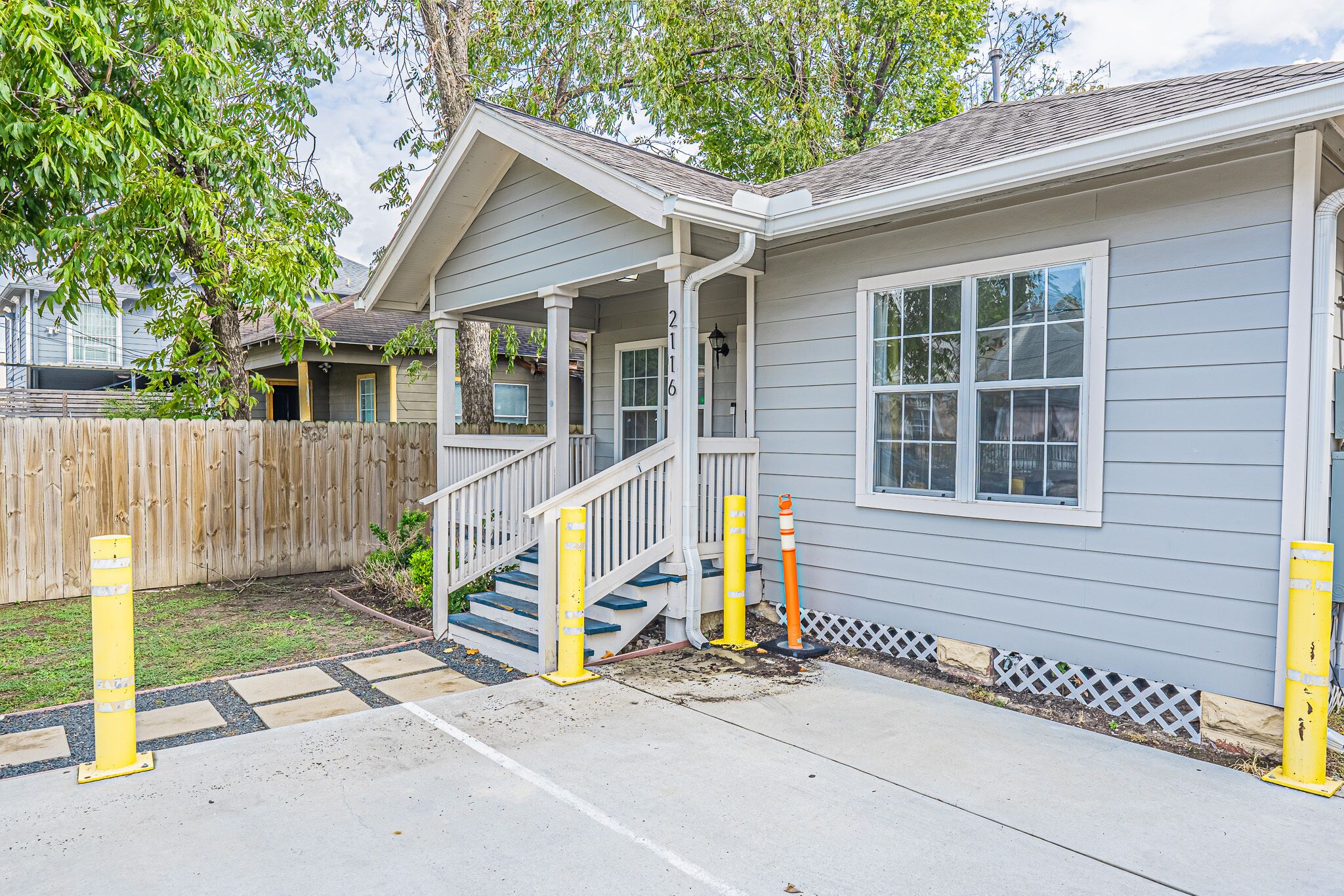 A residential house with a porch, a staircase, and a fenced yard.