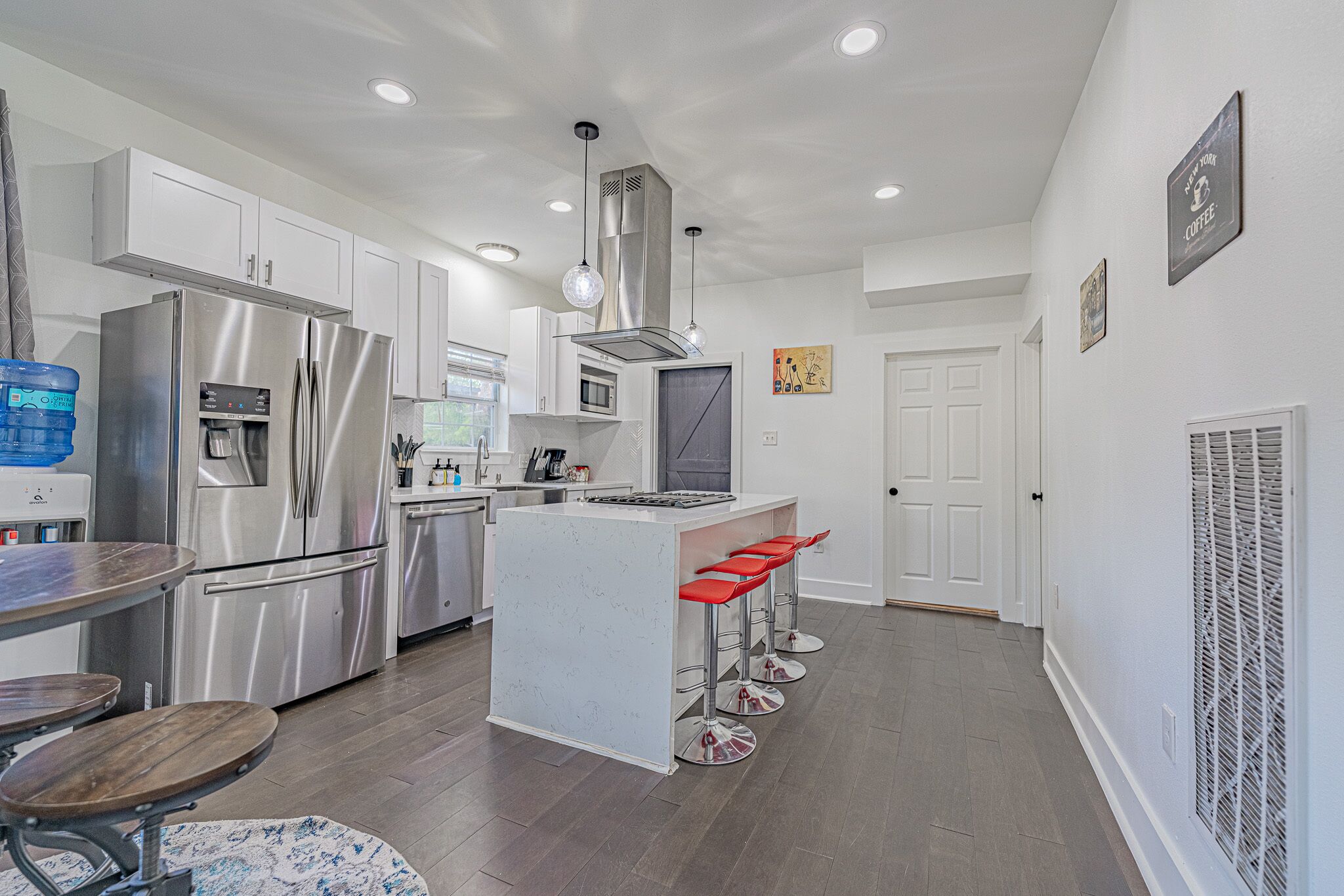 A modern kitchen with stainless steel appliances, a central island with bar stools, and white cabinetry.