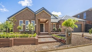 A two-story brick house with a front porch, a garage, and a well-maintained garden with various plants and a small tree.