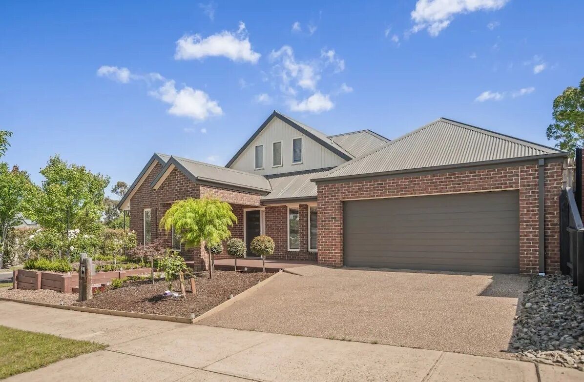 A two-story brick house with a garage, a front yard with landscaping, and a clear blue sky.