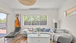 A modern living room with a leather lounge chair, a grey sofa, and a round coffee table. A large window provides natural light and a view of the outdoors.