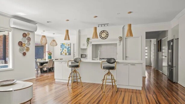 A modern kitchen with white cabinetry, a central island with stools, pendant lighting, and a visible clock.