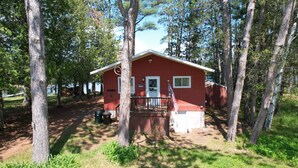 A red cabin with a porch, surrounded by trees.