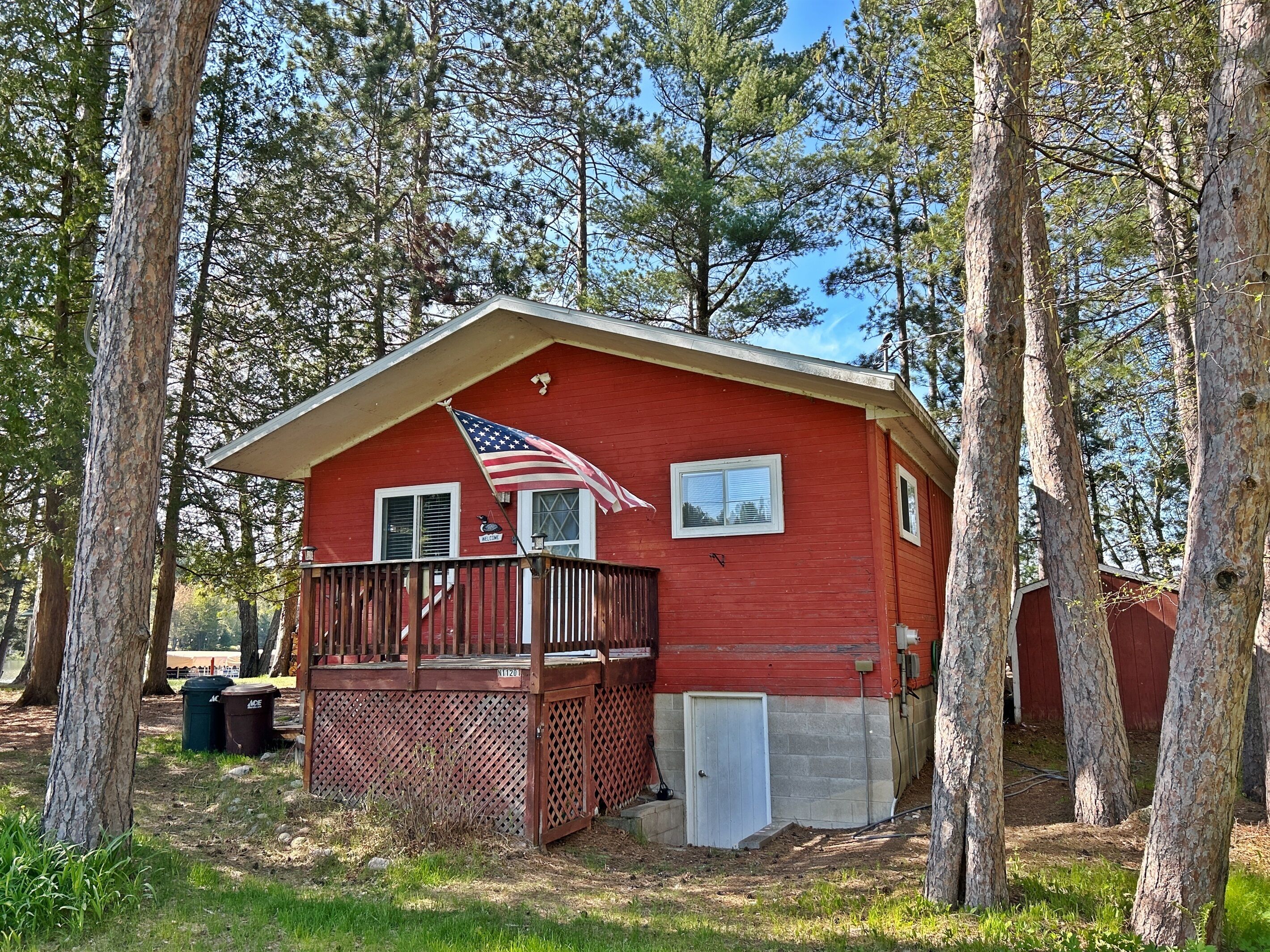 A red cabin with a porch, a small deck, and a flag.