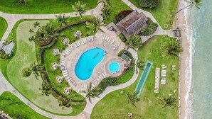 Vue aérienne d’un complexe hôtelier doté d’une grande piscine, de plusieurs espaces de détente, d’un court de tennis et d’une plage.