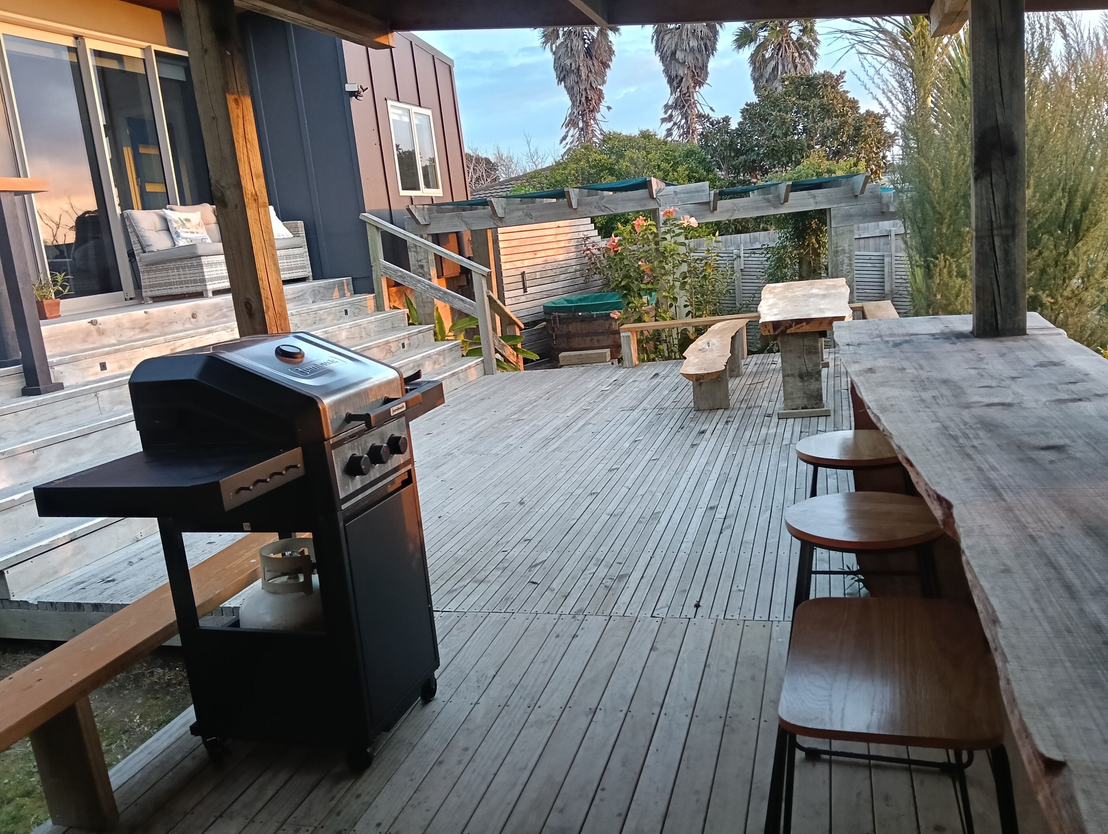 En udendørs terrasse med grill, træbænke og et bord.