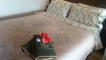 A neatly made bed with floral bedding, a green towel with a red flower, and a small decorative item on the pillow.