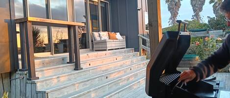 A modern outdoor kitchen with a built-in grill, wooden deck, and a seating area with a sofa and cushions.
