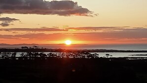 Un atardecer sobre un paisaje costero con siluetas de árboles y colinas al frente.