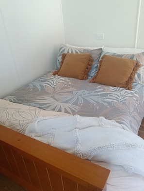 A bed with a floral-patterned bedspread, two brown pillows, and a white throw blanket. - Luxury Beach Bach Karikari (Karikari Peninsula)
