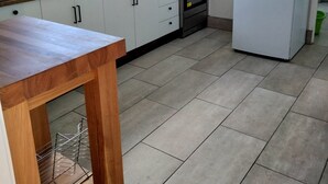 Una cocina con armarios blancos, salpicadero de azulejos, encimera de madera, estufa, horno y refrigerador blanco.