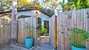 Une clôture en bois, un petit jardin, un chemin et un bâtiment avec une porte sombre.