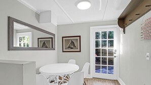 Une pièce avec une table ronde blanche et des chaises, un grand miroir, un tableau encadré et une porte donnant sur l’extérieur.