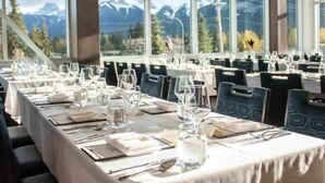 Un ristorante con tavoli apparecchiati per la cena, ampie finestre che offrono vista sulle montagne.