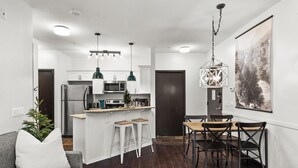Una cucina moderna con mobili bianchi, un'isola centrale e sgabelli da bar. C'è una zona pranzo con un tavolo e sedie in legno.