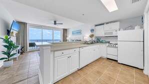 Una cocina moderna con armarios blancos, una isla grande y vistas al océano a través de puertas correderas de vidrio.