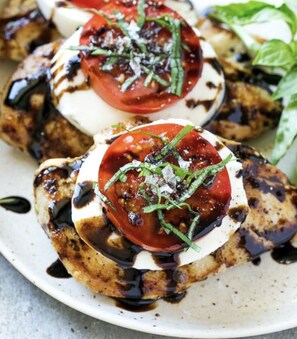 A plate of grilled chicken topped with mozzarella, tomatoes, and basil, drizzled with a balsamic glaze.