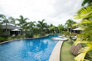 A swimming pool with a curved edge, surrounded by palm trees and lounge chairs.