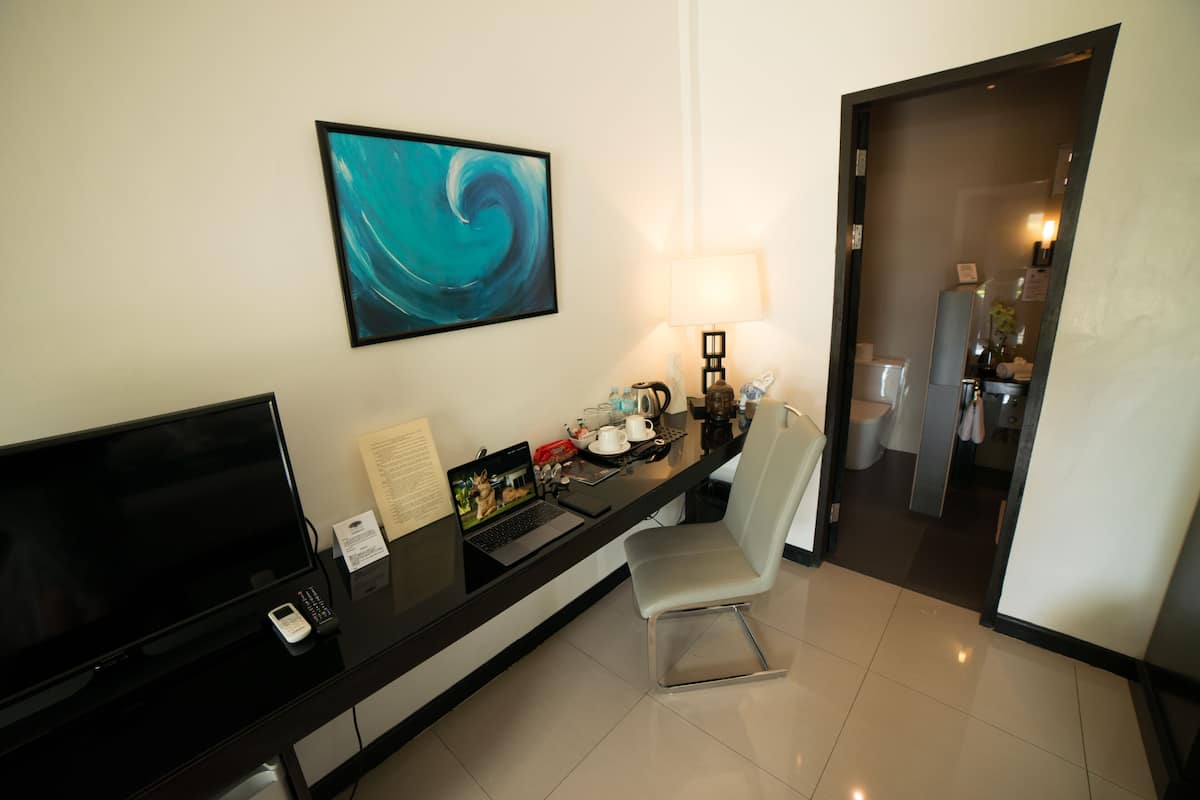 Habitación de hotel con escritorio, laptop, televisión, una silla y un cuadro en la pared.