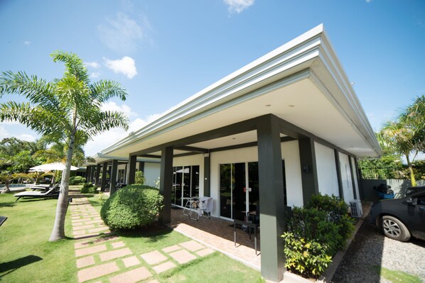 A modern house with a covered patio, a swimming pool, and a well-maintained garden.