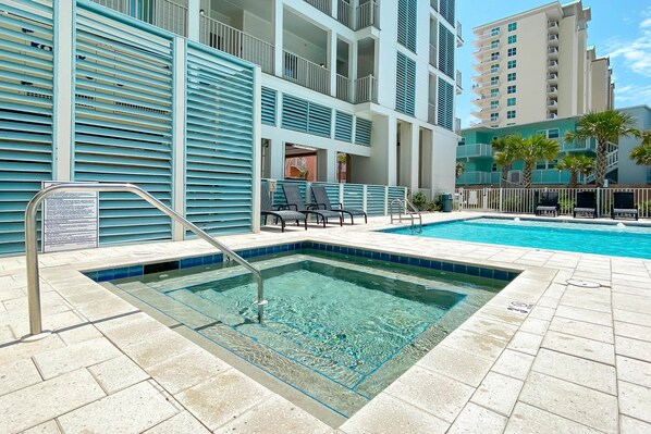 Une piscine à l’eau d’un bleu cristallin, entourée d’une terrasse carrelée et d’un immeuble à plusieurs étages doté de balcons.