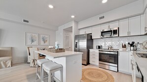 A modern kitchen with white cabinetry, stainless steel appliances, and a central island with bar stools. - DIRECT BEACH ACCESS, GULF VIEWS, ZERO-ENTRY POOL! (Gulf Shores)