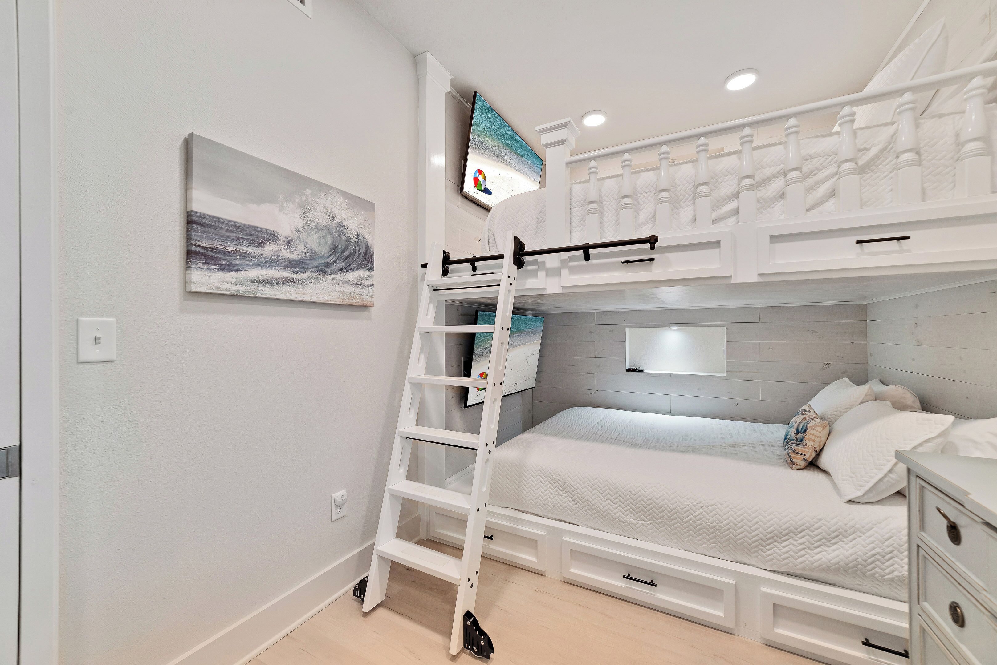 Un dormitorio con literas, una escalera, un televisor y un cuadro.