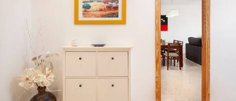Een kamer met een witte kast, een vaas met bloemen, een ingelijst schilderij en een eethoek met stoelen en een tafel.