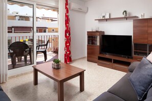 A living room with a TV, wooden furniture, a balcony with a red curtain, and a small plant on a table. - Azucarera Apartment – History and Charm in Torre del Mar (Torre del Mar)