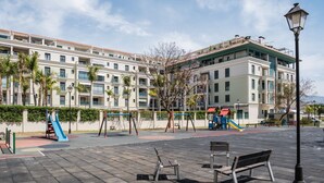 A playground with slides and swings, benches, and a building with balconies in the background.