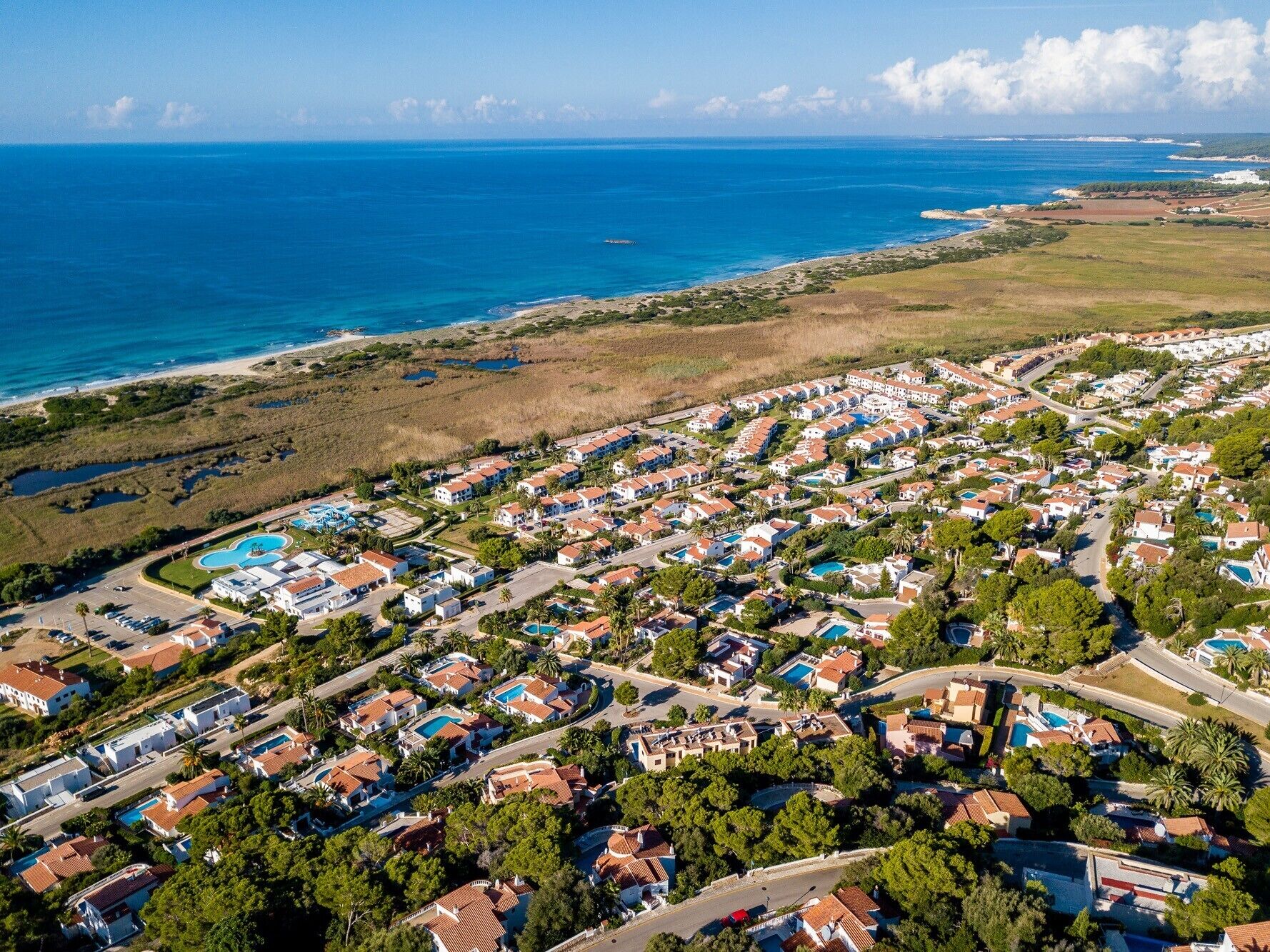 An aerial view of a coastal residential area with houses, roads, and a beach.
