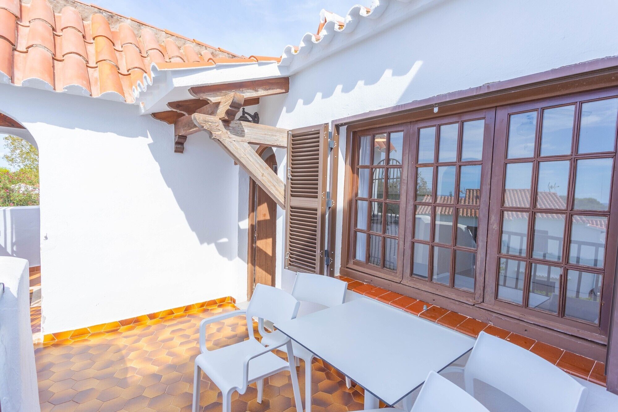 Un patio con tavolo e sedie bianche, una scala in legno e un'ampia finestra a più vetri.