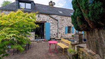 A stone building with a sloped roof, a red table, and a wooden bench in the courtyard.