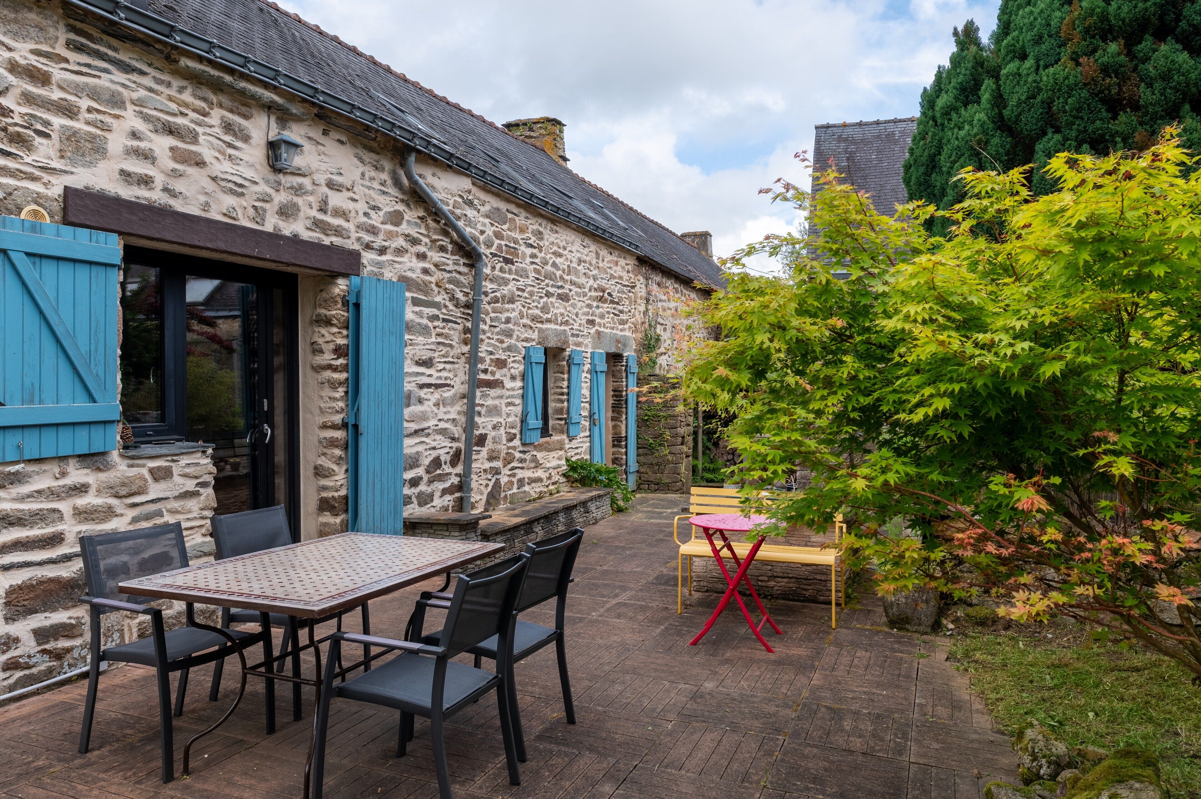 A stone building with a patio, outdoor seating, and a tree.