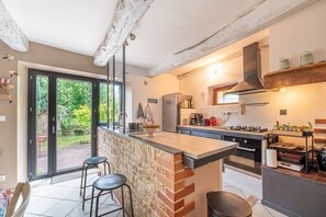 Une cuisine dotée d’un grand îlot central, d’une cuisinière à gaz, d’un four encastré et offrant une vue sur le jardin grâce à une porte-fenêtre coulissante.