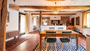 Un comedor rústico con una mesa de madera, sillas verdes y un tapete estampado.