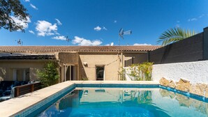 A swimming pool with clear blue water, a tiled deck, and a building with a tiled roof in the background. - Holiday Home 'Loft Des Cigales' with Private Pool and Private Terrace (Uchaud)