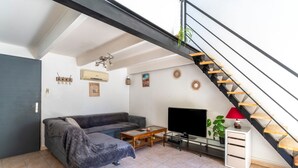 A living room with a sofa, a coffee table, a TV, a staircase, and a small cabinet. - Holiday Home 'Loft Des Cigales' with Private Pool and Private Terrace (Uchaud)