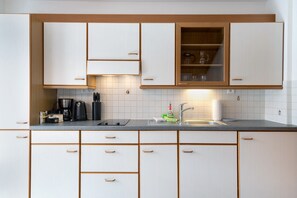 Een keuken met witte kastjes, een aanrecht, een koffiezetapparaat, een waterkoker en een spoelbak.