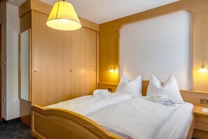 Een hotelkamer met een houten hoofdeinde, een bed met witte lakens, een nachtkastje met een lamp en een spiegel aan de muur.