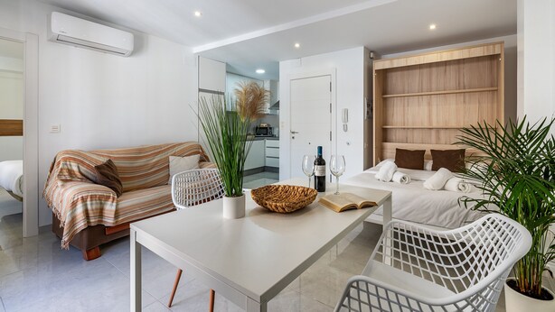 A modern living room with a sofa, a dining table, and a kitchen in the background.