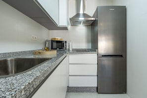 Une cuisine moderne dotée d’appareils électroménagers en acier inoxydable, d’un plan de travail en granit et de meubles blancs.