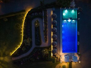 Vue aérienne d’un espace piscine la nuit, avec les aménagements paysagers environnants et un chemin.