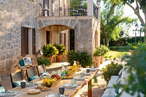 Un espace de restauration en plein air avec des murs en pierre, des meubles en osier et une variété de fruits et de boissons.