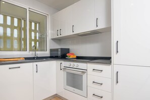 Una cocina con armarios blancos, microondas, horno y ventana con persianas.